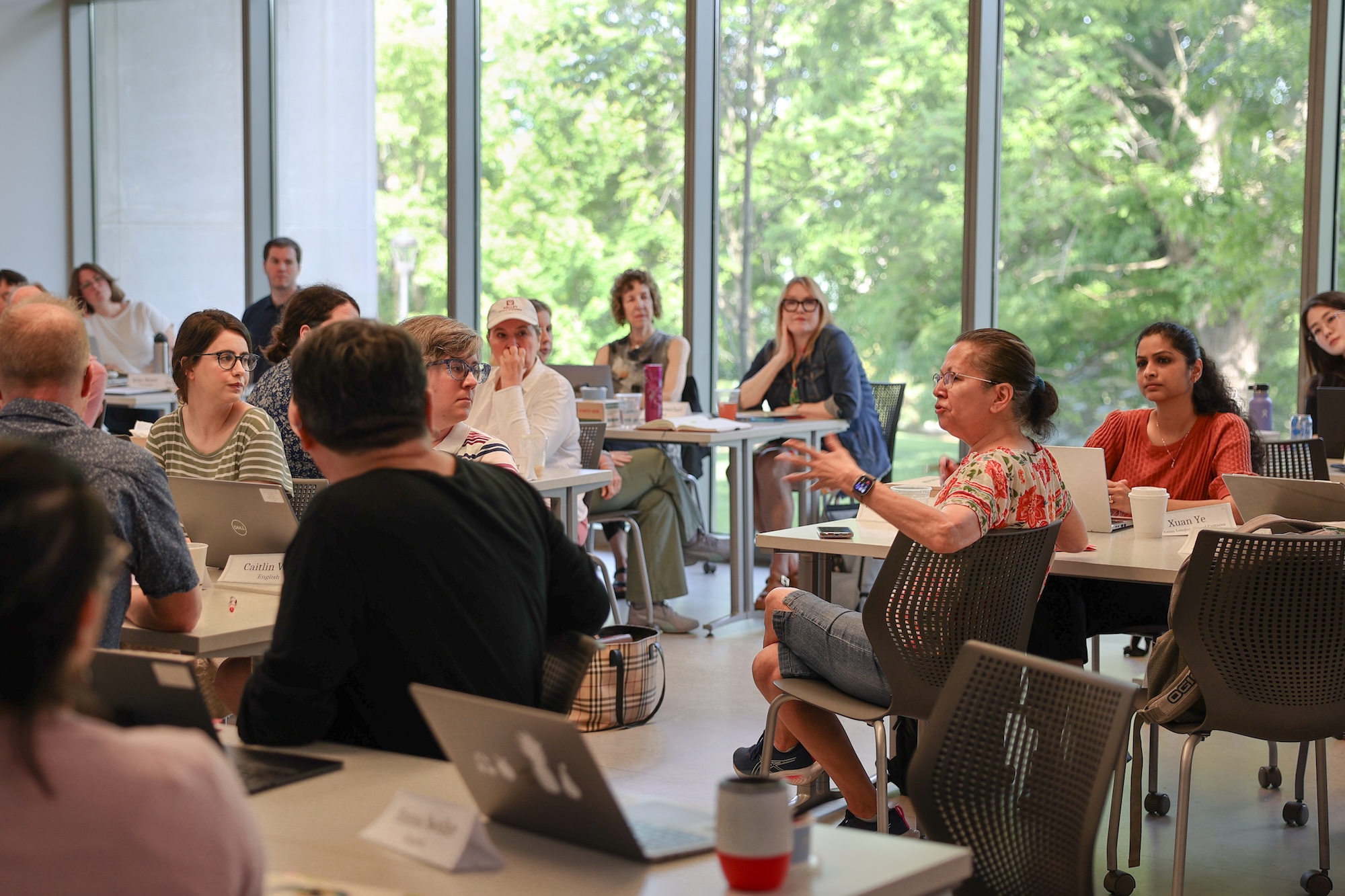 A workshop participant sitting in her chair talks to a room full of colleagues.